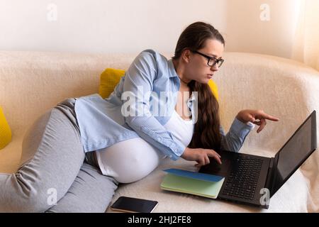 Donna incinta di successo con lavoro duro con laptop e Noutbook. Young Ledy in Pregnancy Work conduce una lezione di conferenza online in remoto Foto Stock