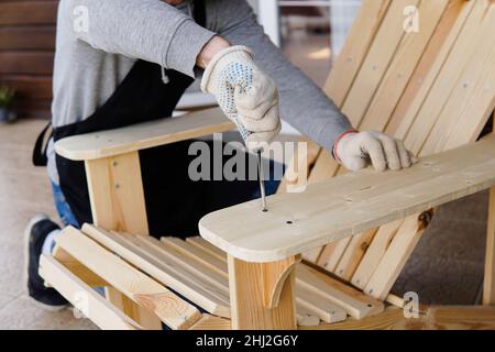 Carpentiere professionale che monta sedia adirondack in legno con cacciavite. Lavoro manuale e fai-da-te Foto Stock