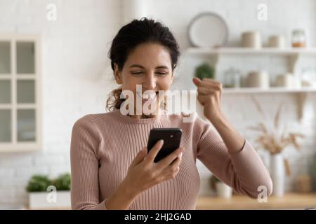 La donna che tiene smartphone gode di buone notizie lette su Internet Foto Stock