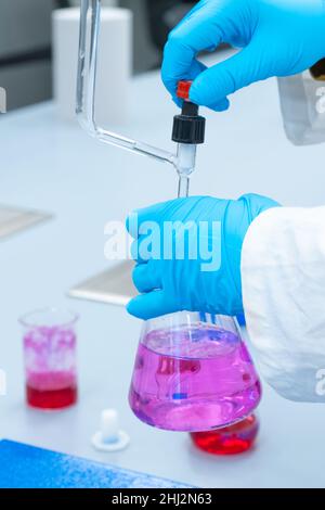 Primo piano l'operatore di laboratorio utilizza un metodo di analisi per la titolazione per studiare le proprietà chimiche del campione d'acqua. Scienziato in possesso di un pallone di Erlenmeyer con soluzione rosa Foto Stock