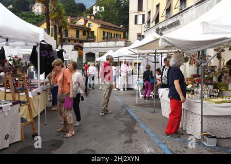 Menaggio, Lago di Como, Italia - Giugno 2019: Persone che guardano merci in mostra in un mercato nel comune di Menaggio sul Lago di Como. Foto Stock