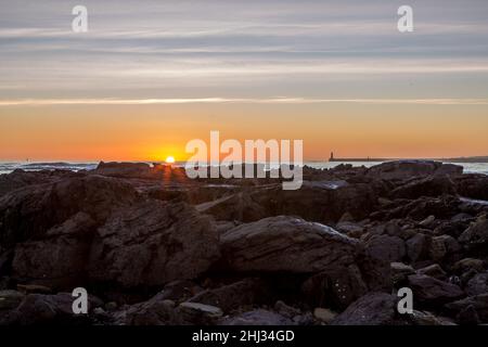 Alba sulla spiaggia Longsands di Tynemouth mentre il sole appare all'orizzonte sopra le rocce Foto Stock