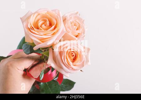 Mano dell'uomo che tiene un bouquet di belle rose rosa su uno sfondo chiaro con spazio di copia. San Valentino, festa della mamma, concetto di buon compleanno. ROM Foto Stock