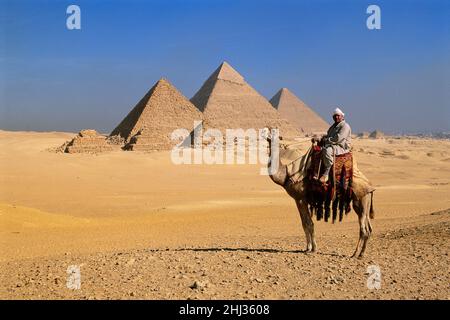 Uomo a cavallo di un cammello di fronte alle piramidi di Giza, Giza, Egitto Foto Stock