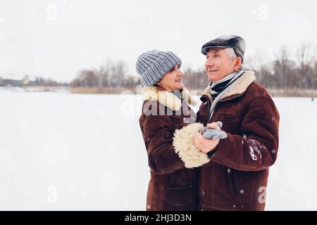 Coppia di famiglie anziane che ballano all'aperto durante il clima invernale nevoso. Persone anziane che si divertono a camminare. San Valentino Foto Stock
