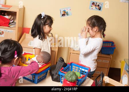 Istruzione le ragazze prescolare che giocano in famiglia fingono area di gioco, una giocando con la bambola e le altre due giocando con una macchina fotografica, parlando una foto Foto Stock