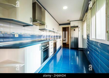 Cucina con un sacco di mobili, piano di lavoro blu, lavandino in acciaio inox e piastrelle blu pavimenti e pareti Foto Stock