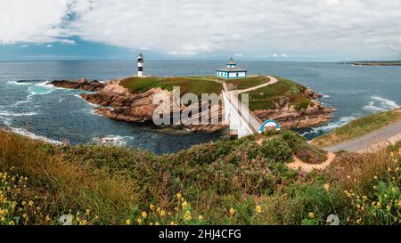 Faro su una piccola isola rocciosa al largo della costa collegata ad essa da un piccolo ponte. Foto Stock