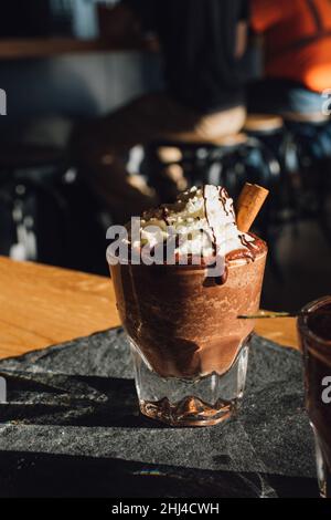 cioccolata calda bevente con panna montata, gocce di cioccolato e cannella bastone nel caffè Foto Stock