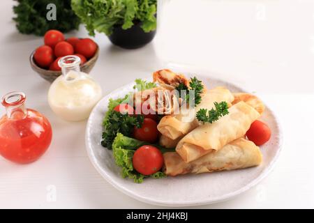 Rotoli di Primavera fritti profondi, popolari come Lumpia o Popia. Servito su piatto bianco, tavolo bianco con salsa piccante e maionese. Spazio copia per testo Foto Stock