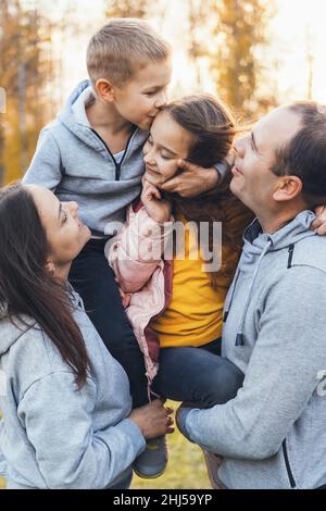 Famiglia di quattro in posa per album di famiglia, genitori che tengono figlio e figlia in armi, baciare e abbracciare. Buona famiglia che passa il tempo insieme. Foto Stock
