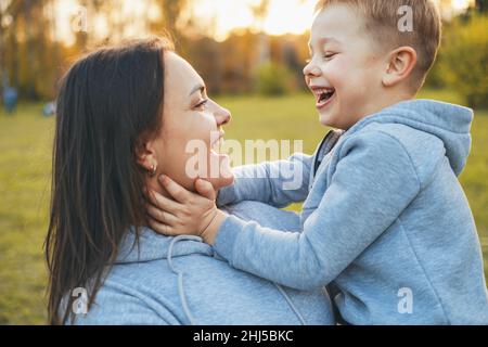 Ritratto laterale di un ragazzo che guarda negli occhi della madre mentre gioca con le mani che toccano il volto della madre. Vista ravvicinata. Tenere le mani Foto Stock