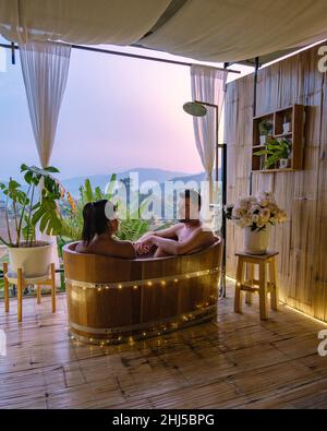 Vasca da bagno durante il tramonto sulle montagne di Chiang mai Thailandia, rilassante in legno caldo vasca idromassaggio fuori nel deserto. Bagno rilassante, coppia uomo e donna in vasca Foto Stock