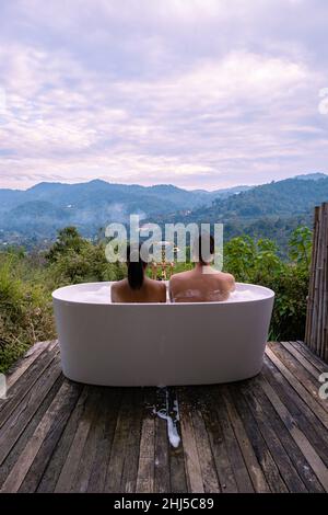 Vasca da bagno durante il tramonto sulle montagne di Chiang mai Thailandia, rilassante in legno caldo vasca idromassaggio fuori nel deserto. Bagno rilassante, coppia uomo e donna in vasca Foto Stock