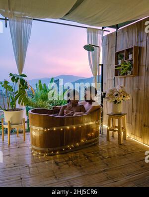 Vasca da bagno durante il tramonto sulle montagne di Chiang mai Thailandia, rilassante in legno caldo vasca idromassaggio fuori nel deserto. Bagno rilassante, coppia uomo e donna in vasca Foto Stock