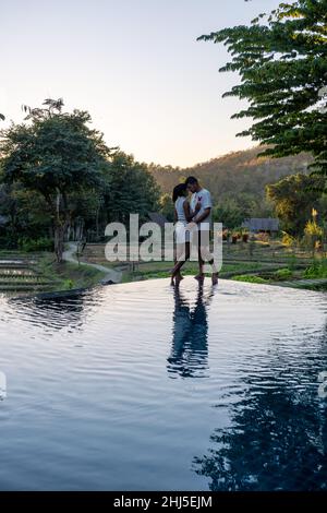 Coppia uomo e donne che guardano il tramonto su un bordo di una piscina con una vista sulle montagne e risaie del nord Thailandia Mae Hong Son. Foto Stock