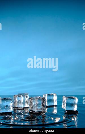 Cubetti di ghiaccio in acqua blu brillante e un tuffo di gocce di pioggia Foto Stock