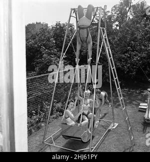 Una nuova macchina acrobatica è stata ideata da 'The Amazing Briton and His West End Lovelies'. Si tratta di una barca altalena umana che sarà mostrata per la prima volta al Carnevale annuale presso il parco di Gloucester. L'incredibile Briton si aggancia alla schiena delle gambe tenendole con le mani su una barca con due ragazze e le fa oscillare verso l'alto e verso il basso. Nella foto, il 'Amazing Briton' sul ponteggio che tiene in barca, il biondo Judy Cornford e la bruna Monica Buchanan. La barca viene spinta dalla moglie Peggy Briton. 27th luglio 1956. Foto Stock