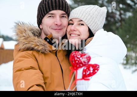 Un uomo e una donna innamorati in un appuntamento all'aperto in inverno nella neve con un arredamento rosso a forma di cuore. San Valentino, amore, felice coppia in lo Foto Stock