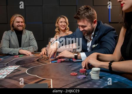 Ragazzo allegro bearded seduto al tavolo da poker nel casinò e fare la scommessa Foto Stock