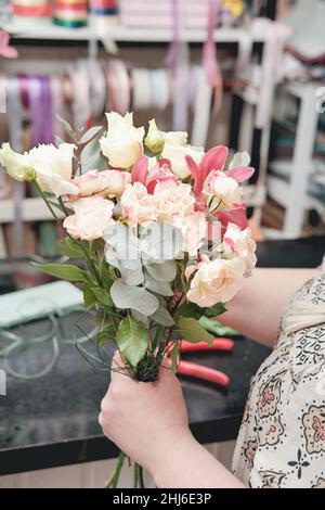 fiorista donna che fa delicato bouquet di nozze per una sposa. eucaliptus foglie, rose piccole e orchidea in mani fioriste Foto Stock