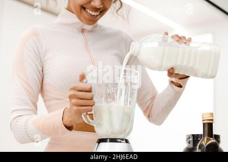 Giovane donna nera che sorride e fa frullato con il latte a casa Foto Stock