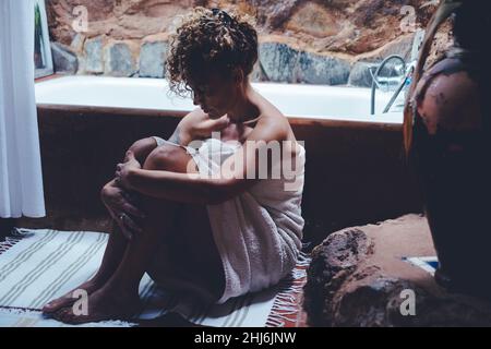 Donna adulta seduta sul pavimento in bagno a casa dopo abuso o depressione malattia. Le donne stressate al coperto tristi a terra. Signora abbracciante Foto Stock