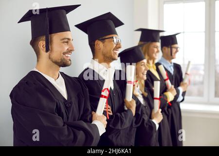 I laureati sorridenti in fila posano con i diplomi Foto Stock