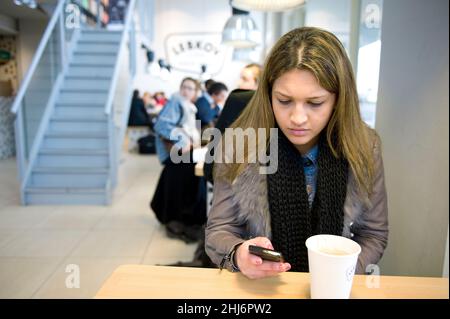 Rotterdam, Paesi Bassi,. Giovane donna adulta che controlla i messaggi dello smartphone mentre si fa un caffè al Lebkov Coffee Place. Foto Stock