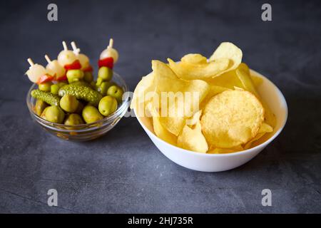 Una ciotola bianca con patatine e una ciotola di vetro con brocette spagnole su sfondo nero di ardesia Foto Stock