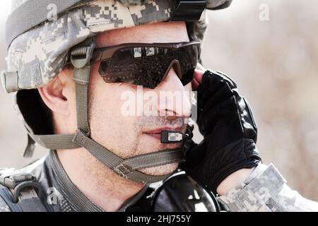 Mantenere la comunicazione al comando. Profilo closeup di un soldato che comunica con la sua cuffia. Foto Stock