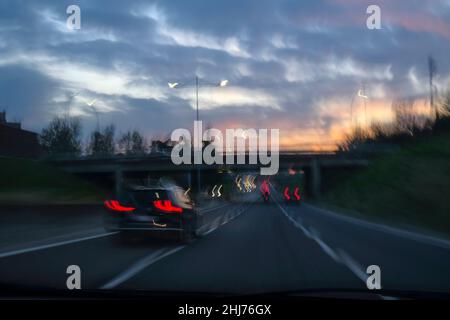 Tramonto sfocato sull'autostrada piena di auto attraverso il ponte e cielo pieno di nuvole. Viaggio, viaggio. Movimento delle auto in movimento. Luci sfocate, sfocate Foto Stock