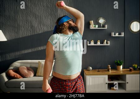 Comico uomo grasso serio esercitandosi con i pesi Foto Stock