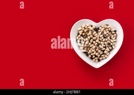 Legumi assortiti non cotti in forma di cuore piatto su sfondo rosso Foto Stock
