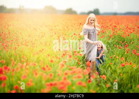 Famiglia felice riposato su un bel campo di papavero al tramonto. Mamma e figlia corrono intorno al prato che tiene le mani. Famiglia divertirsi. Foto Stock