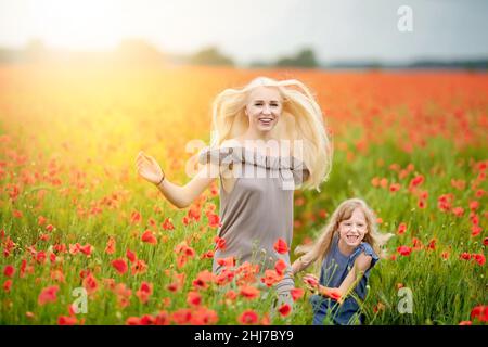 Famiglia felice riposato su un bel campo di papavero al tramonto. Mamma e figlia corrono intorno al prato che tiene le mani. Famiglia divertirsi. Foto Stock