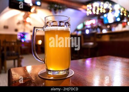 Riposo. Un bicchiere di birra lager in legno nella calda luce del bar. Alcol, intrattenimento, bevande tradizionali, concetto di atmosfera Oktoberfest. Foto Stock