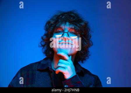 Ritratto di giovane uomo felice, studente in camicia nera sorridente isolato su sfondo blu in neon. Concetto di emozioni, studio, educazione, moda Foto Stock