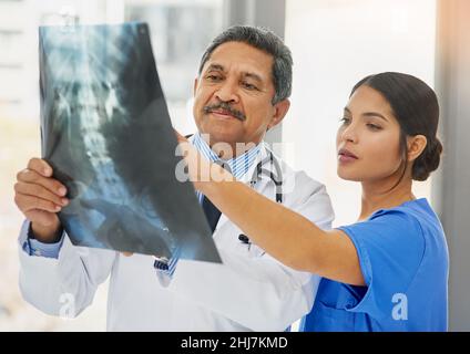 Vedere fino al problema. Shot di un medico maturo e di una giovane infermiera che guardano insieme una radiografia. Foto Stock