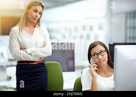 Catturato nell'atto. Scatto corto di una giovane donna d'affari catturato su una chiamata personale durante le ore di lavoro. Foto Stock