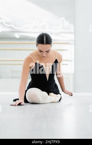 ballerino giovane in abito nero che si estende sul pavimento in studio balletto Foto Stock