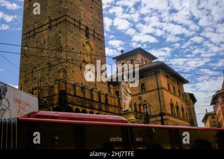 Statua di San Petronio attraverso le due torri, autobus in movimento e cielo blu, Bologna, Italia Foto Stock
