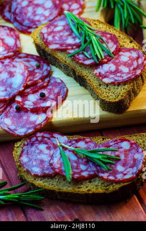 sandwich con salsiccia su un asse di legno e spezie primo piano Foto Stock