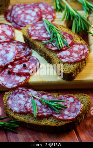 sandwich con salsiccia su un asse di legno e spezie primo piano Foto Stock