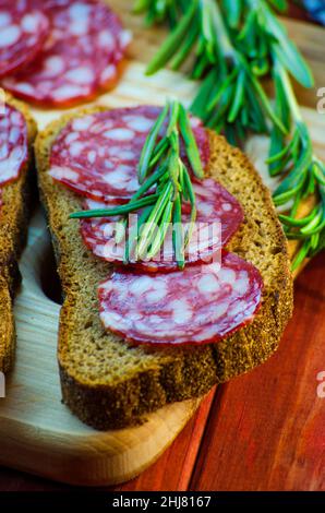 sandwich con salsiccia su un asse di legno e spezie primo piano Foto Stock