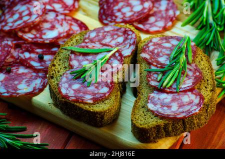 sandwich con salsiccia su un asse di legno e spezie primo piano Foto Stock