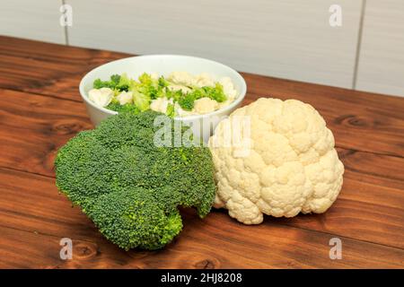 Ciotola bianca riempita con fiori di broccoli e cavolfiore con teste di broccoli e cavolfiore poste su fondo di legno di quercia Foto Stock