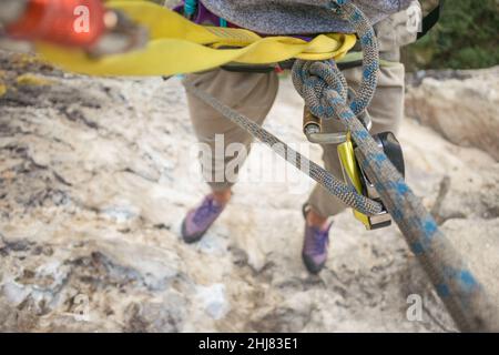POV: Scalatore di roccia appende dalla corda e dall'ingranaggio alto sopra il terreno Foto Stock