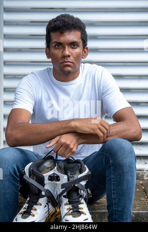 Ritratto di giovane uomo di latino sicuro con t-shirt e pattini in linea. Foto Stock