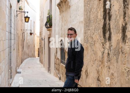 Ritratto di un uomo bianco di 42 anni fiducioso e rilassato in piedi in una stretta strada vecchia Foto Stock